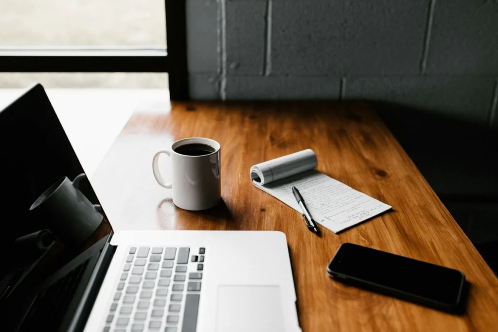 Laptop, coffee mug, and notepad on a wooden desk. A realistic workspace setup for side gig entrepreneurs wanting side gigs without hype or distraction.