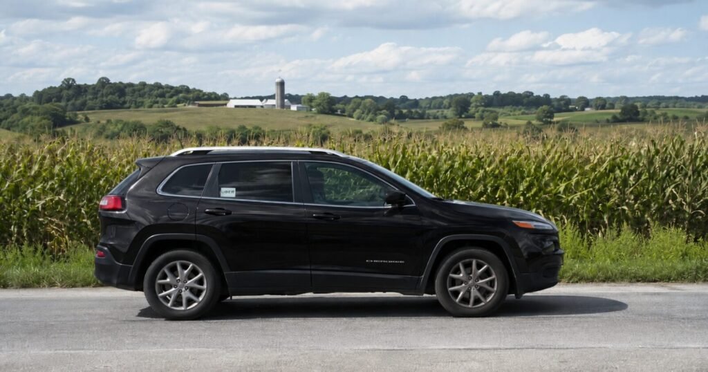 Black Jeep Cherokee used for Uber driving parked beside a cornfield in a rural area.