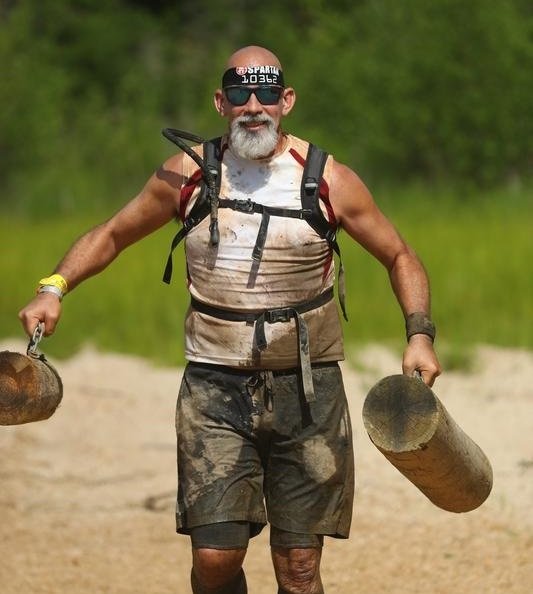 Brian carrying heavy logs during a muddy obstacle-course race.